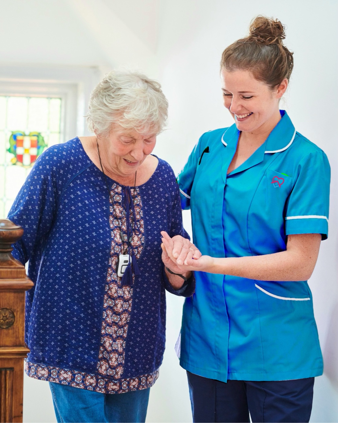 A carer in a vivid azure Help to Live tunic offering gentle support to an older woman